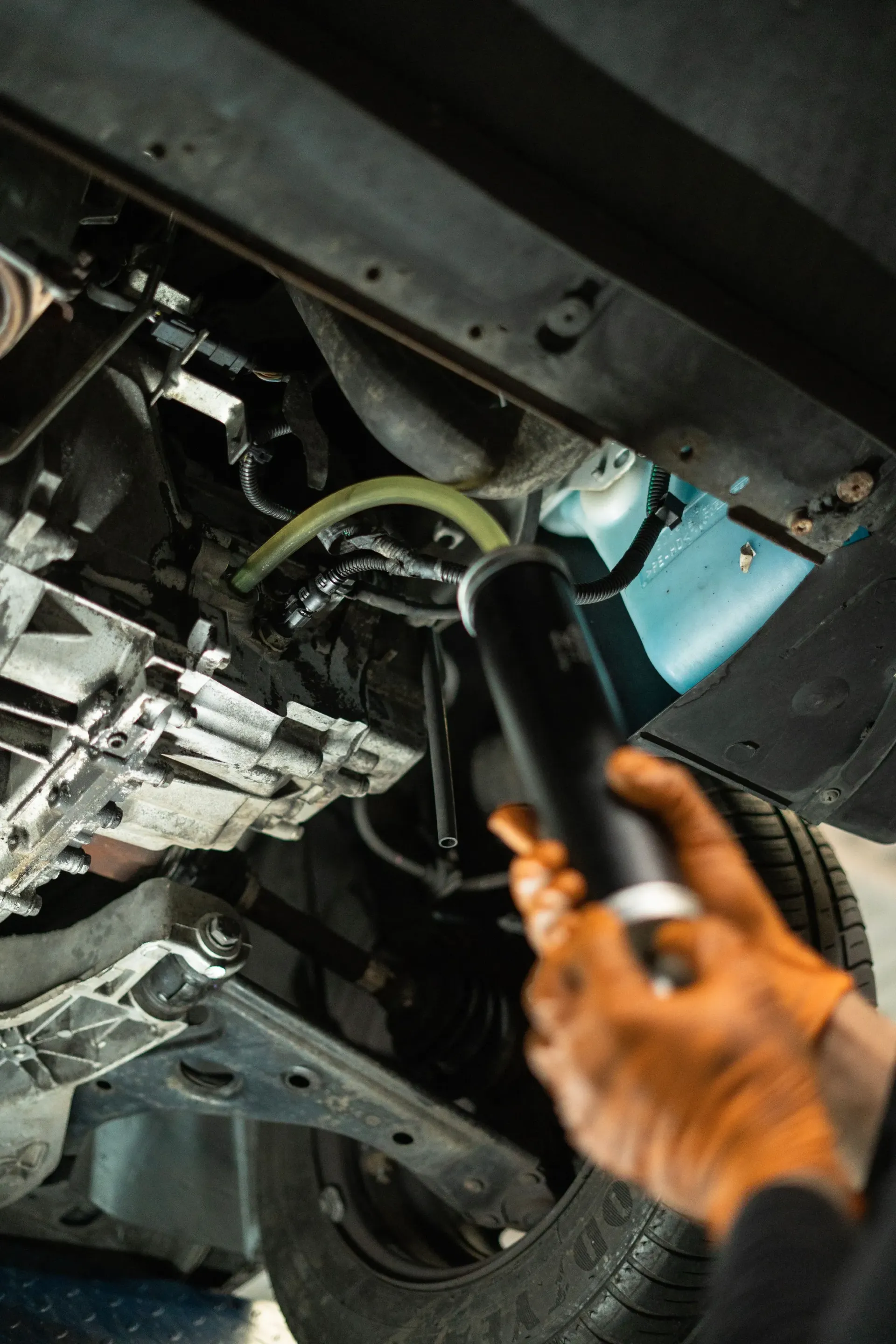 Mecánico utilizando una luz debajo de un coche, iluminando los componentes del chasis y un tubo transparente.