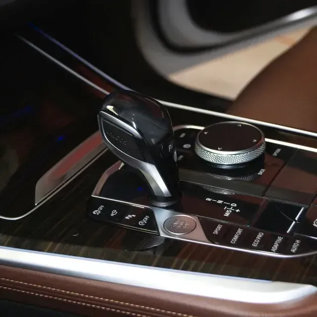 Palanca de cambios y panel de control del coche con dial giratorio y botones en una consola de madera.