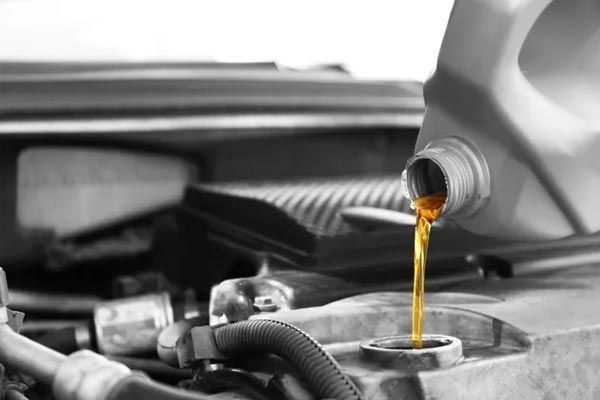 Verter aceite de motor en un motor de coche. La escena está en blanco y negro, excepto el aceite, que es de color marrón dorado.