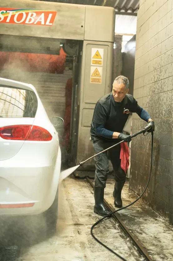 Un hombre lava un coche blanco con una manguera de alta presión en un lavadero de coches.