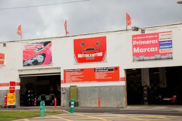 Taller de reparación de automóviles Autocentro con bahías abiertas, letreros y detalles en naranja.