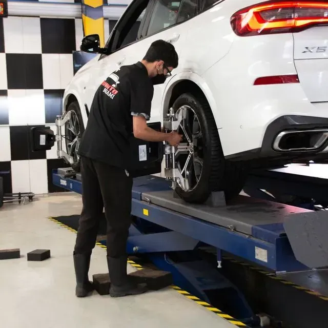 Mecánico ajustando la alineación de las ruedas de un SUV blanco en un taller mecánico.