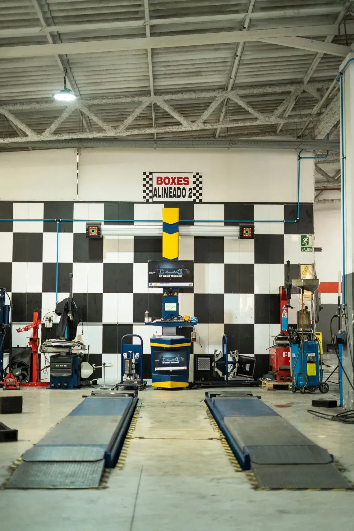 Taller de reparación de automóviles con elevador de alineación y pared en forma de tablero de ajedrez.