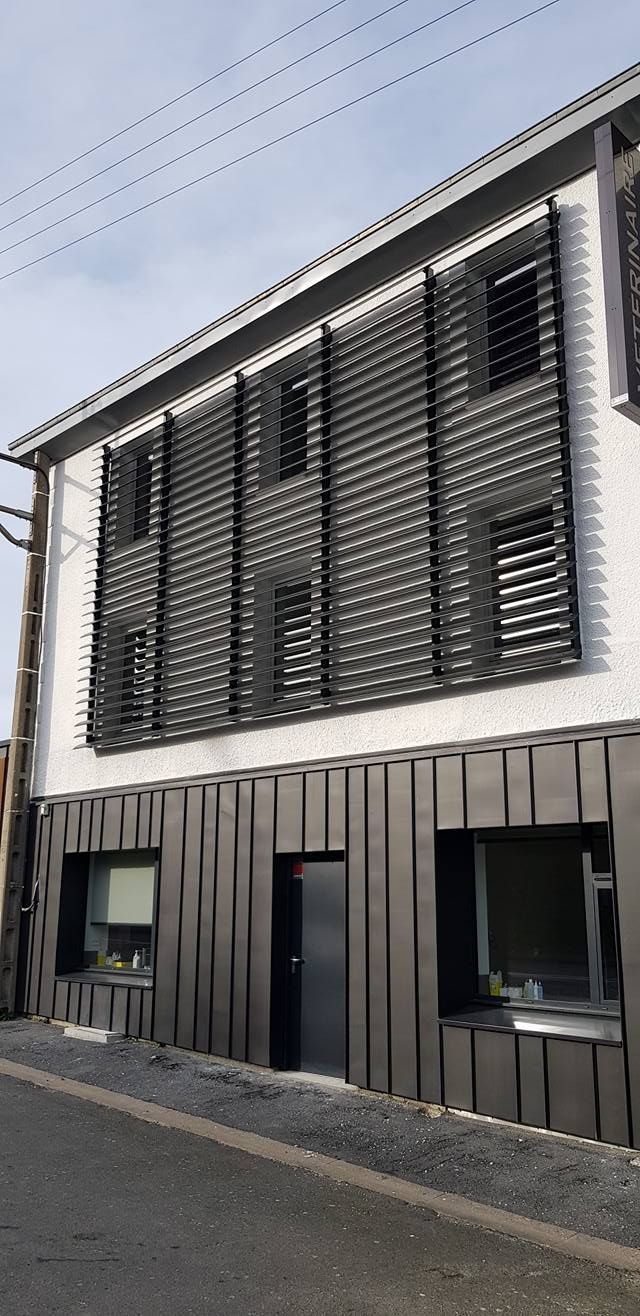 Un bâtiment moderne avec une façade supérieure blanche ornée de panneaux horizontaux sombres et une base sombre à panneaux verticaux.