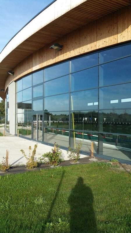 Bâtiment moderne aux formes courbes, doté d'une grande façade vitrée, d'un toit en bois en avant-toit et d'une pelouse au premier plan.