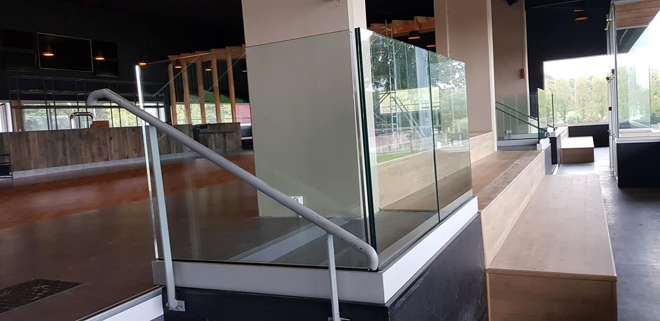Vue intérieure d'un bâtiment moderne montrant un escalier avec une balustrade en verre et une main courante menant à un coin salon.