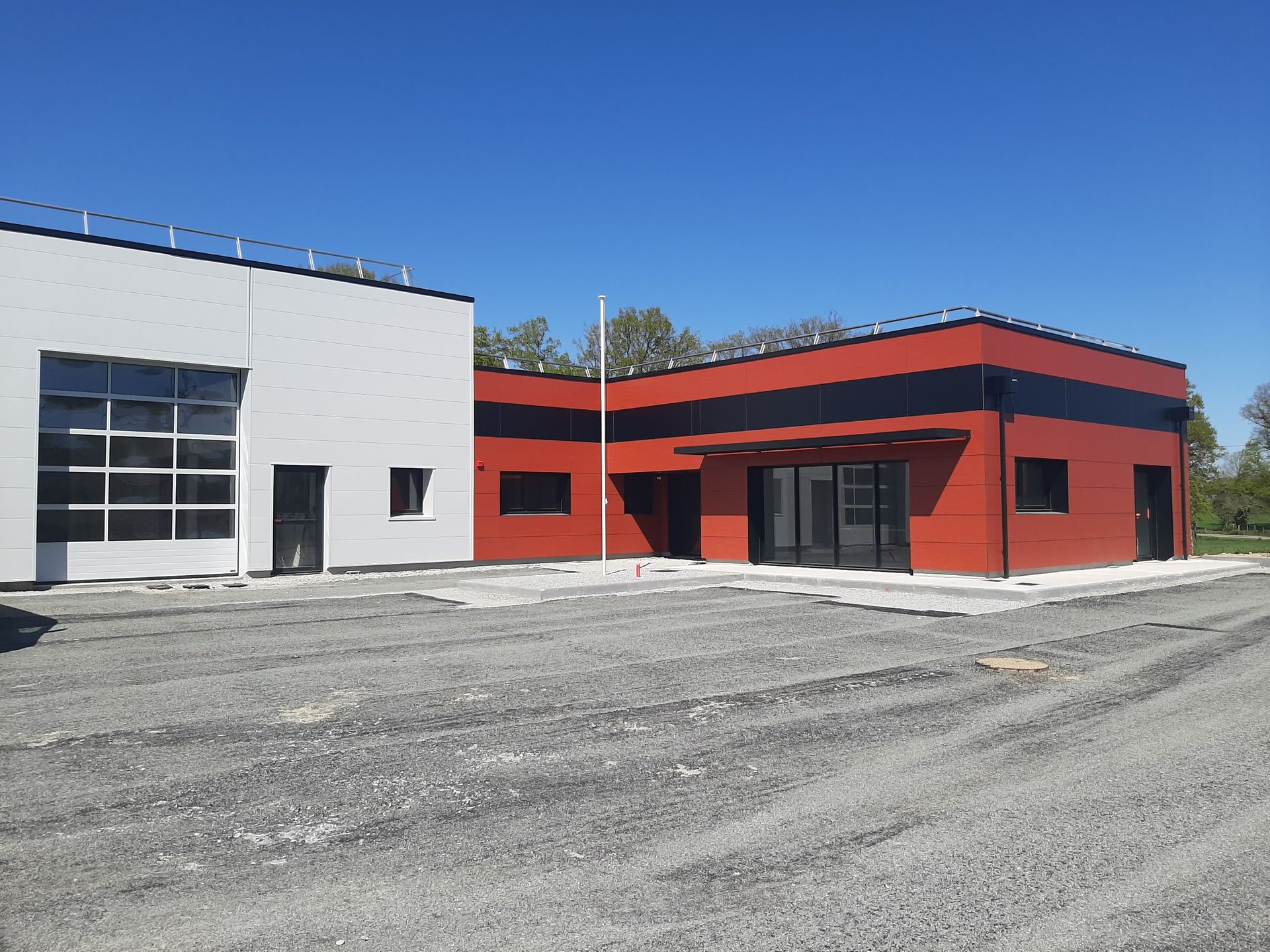 Un bâtiment moderne aux parties blanches et rouges se détachant sur un ciel bleu clair, sur un sol de gravier.