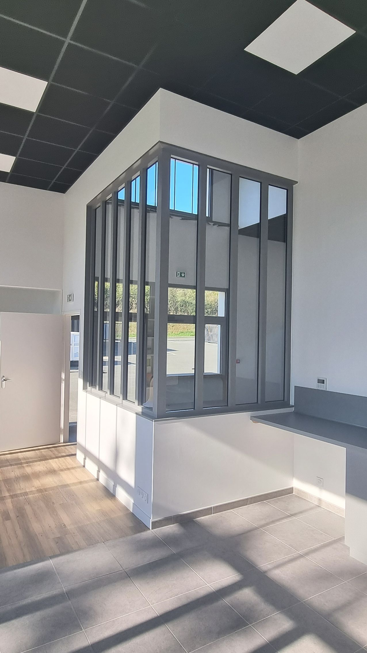 Vue intérieure d'un espace commercial avec une cloison à ossature métallique grise en construction contre un mur blanc.