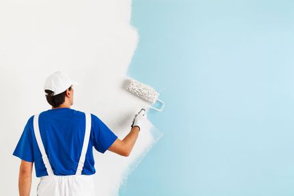 Maler in blauer Uniform streicht mit einer Rolle eine weiße Wand blau.