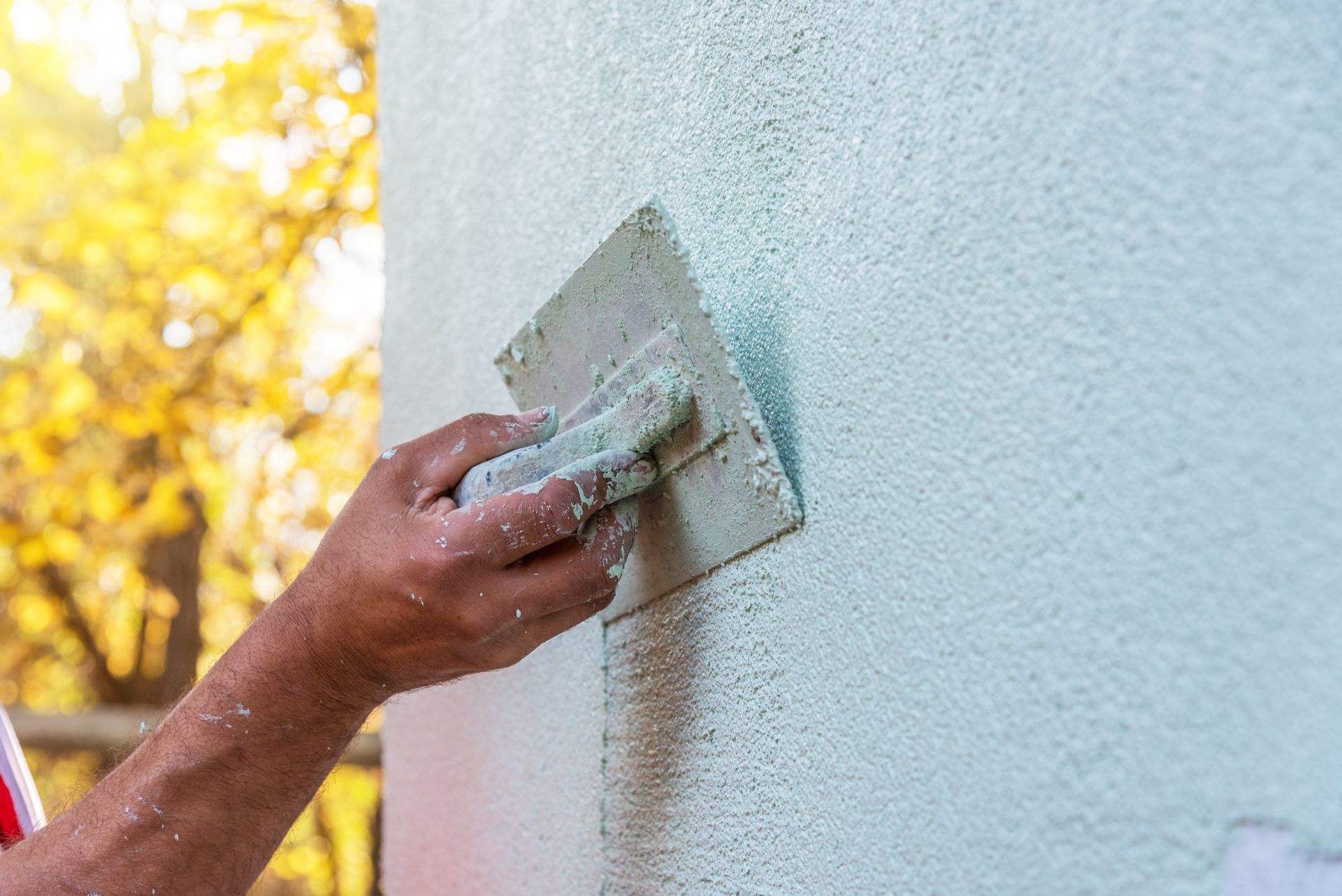 Eine Person trägt mit einem Spachtel weiße Trockenbaumasse auf eine Wand auf.