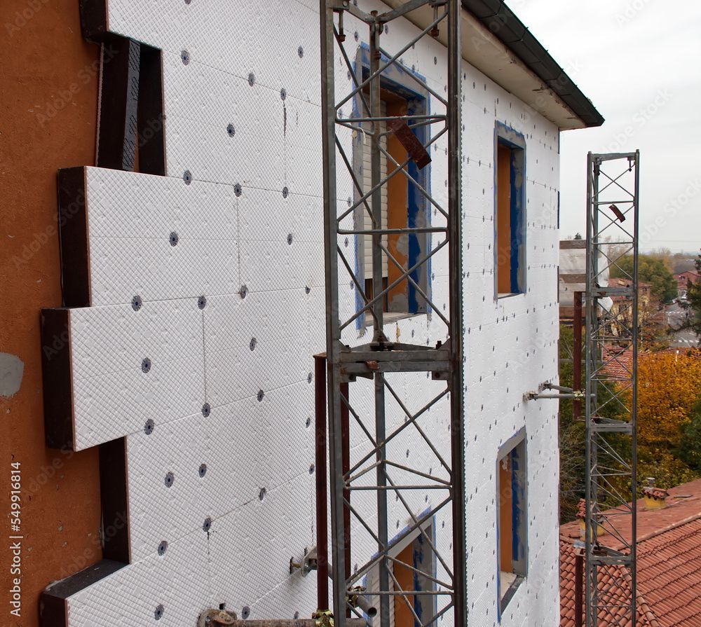 Außendämmung eines Gebäudes. An der Wand sind weiße Dämmplatten angebracht, davor ein Metallgerüst.
