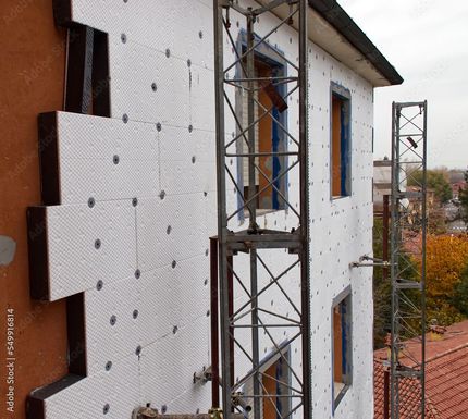 Gebäudeaußenseite mit weißen Dämmplatten, Gerüst und sichtbaren Fensterrahmen.