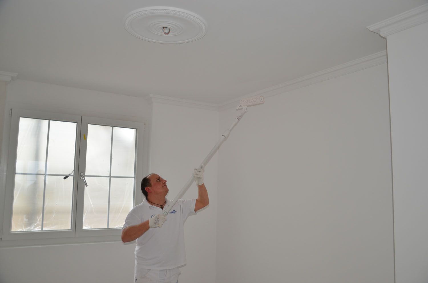 Maler in blauer Uniform streicht mit einer Rolle eine weiße Wand blau.