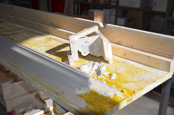 Eine Gipsleiste in einem Holzrahmen auf einem gelben Tisch, mit einem Eckstück aus Gips.