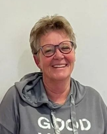 Frau mit Brille lächelt und trägt einen grauen Kapuzenpullover mit der Aufschrift „GOOD VIBES“.