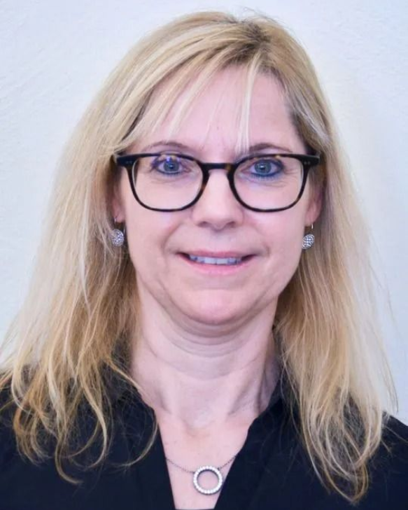 Frau mit Brille lächelt und trägt einen grauen Kapuzenpullover mit der Aufschrift „GOOD VIBES“.