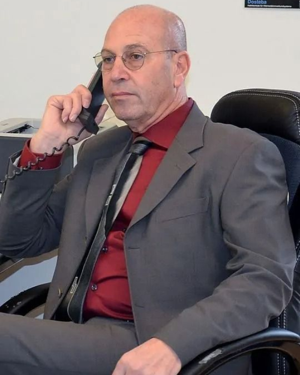 Mann im Anzug, telefoniert, sitzt an einem Schreibtisch. Rotes Hemd, grauer Anzug, Brille.