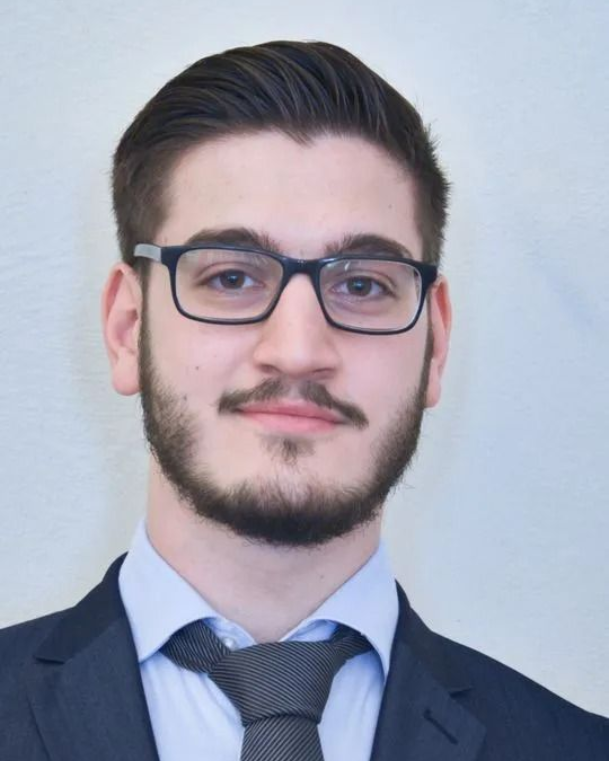 Junger Mann mit Brille, Spitzbart und Krawatte, im Jackett, lächelt in die Kamera.