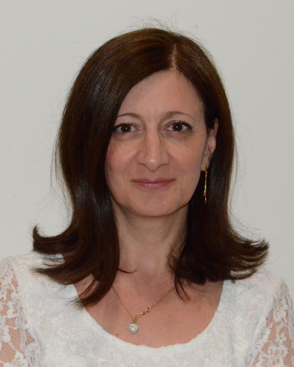 Frau mit braunem Haar, lächelnd, trägt Ohrringe, vor weißem Hintergrund.