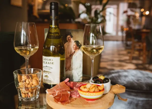 Een fles wijn, glazen, een charcuterieplank met hapjes en een foto op tafel.