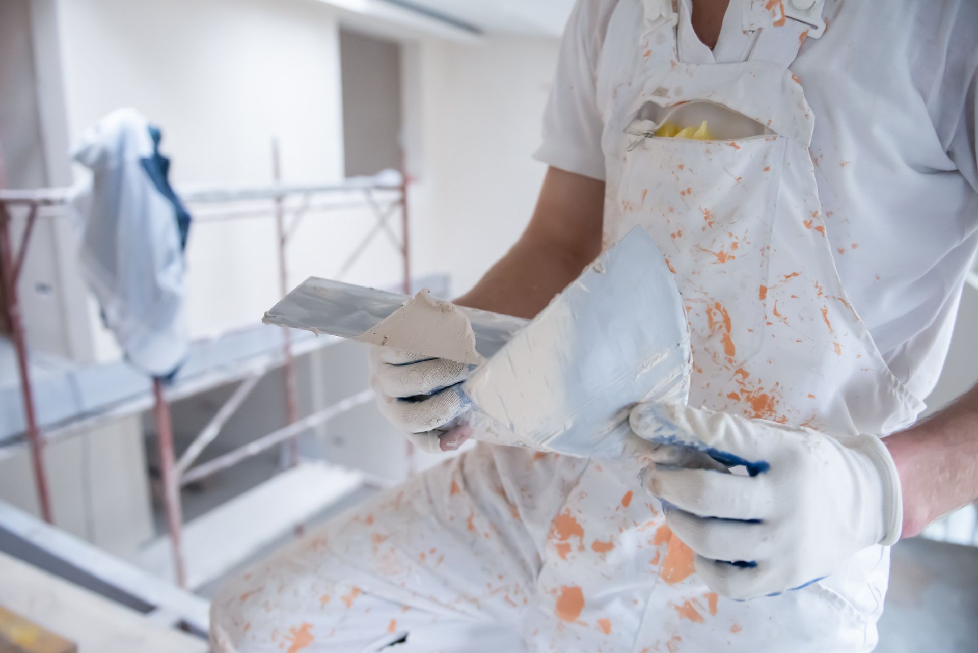 Pintor sosteniendo dos espátulas, cubiertas de pintura, en un entorno de construcción.
