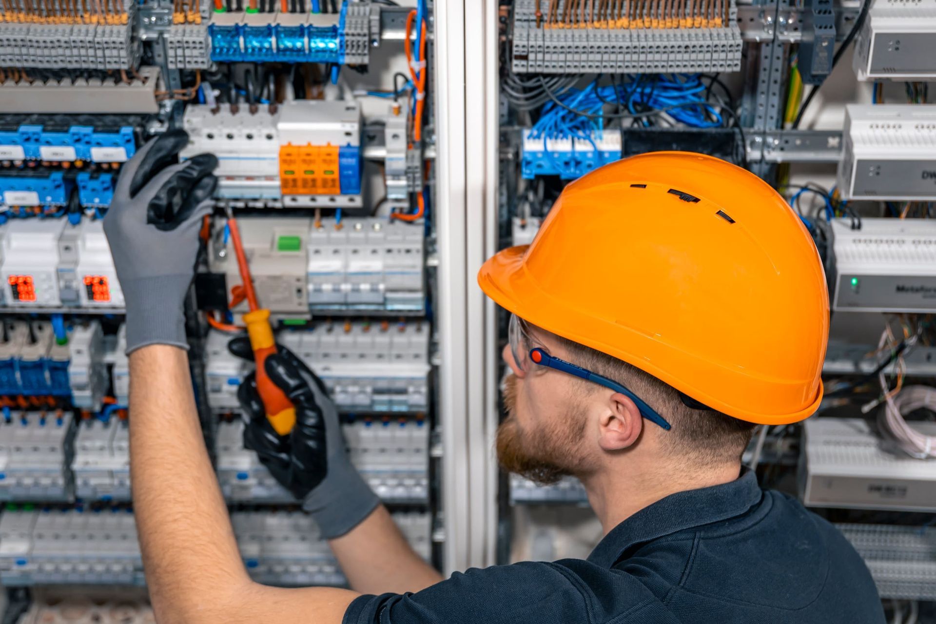 Electricista con casco naranja trabajando en un panel eléctrico.