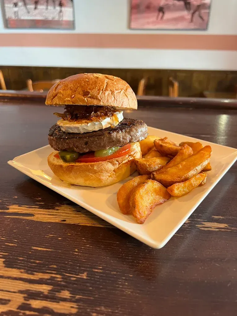 Hamburguesa con queso de cabra, tomate y patatas fritas en plato.