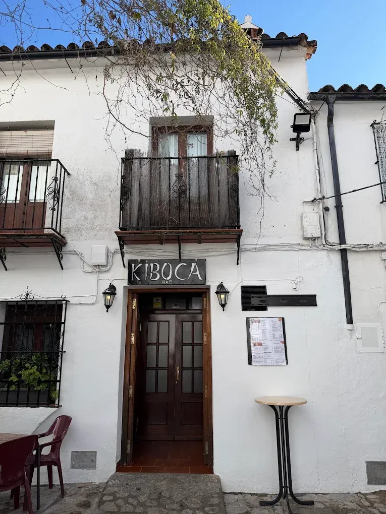 Edificio blanco con puerta marrón abierta, balcón y letrero