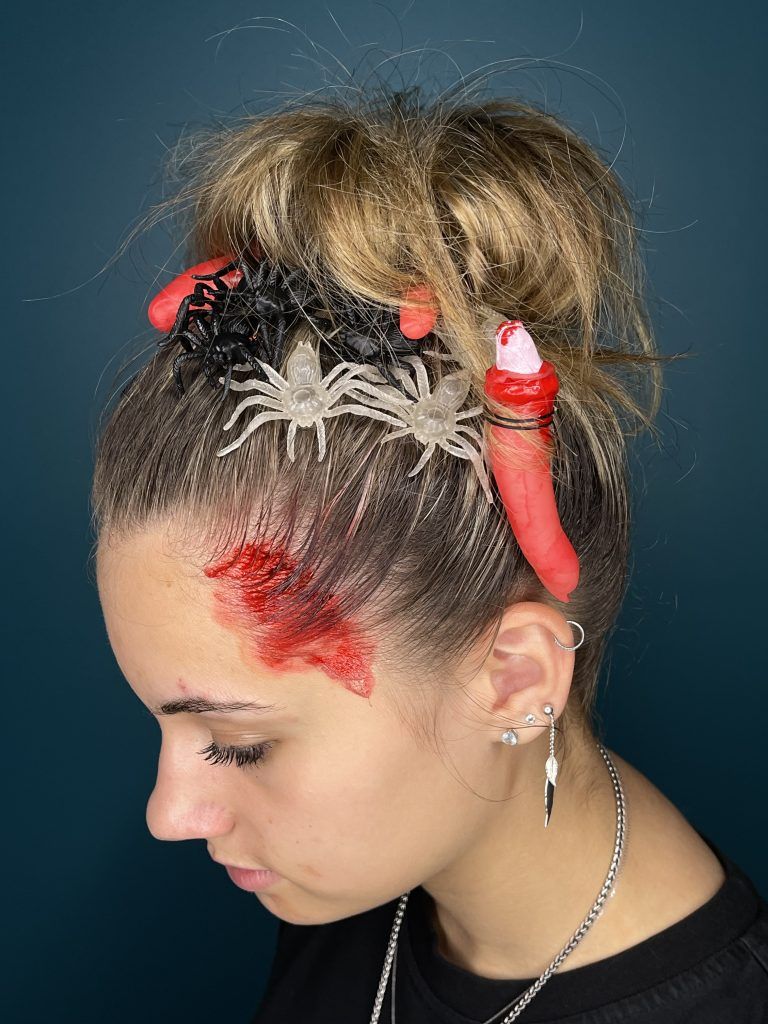 Profil d'une personne avec une coiffure tressée, des barrettes rouges et une marque rouge sur le front, sur fond bleu.