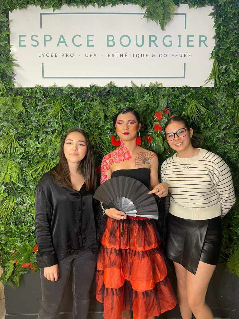 Trois personnes posent devant un mur vert et le panneau Espace Bourget, l'une d'elles tenant un éventail noir.