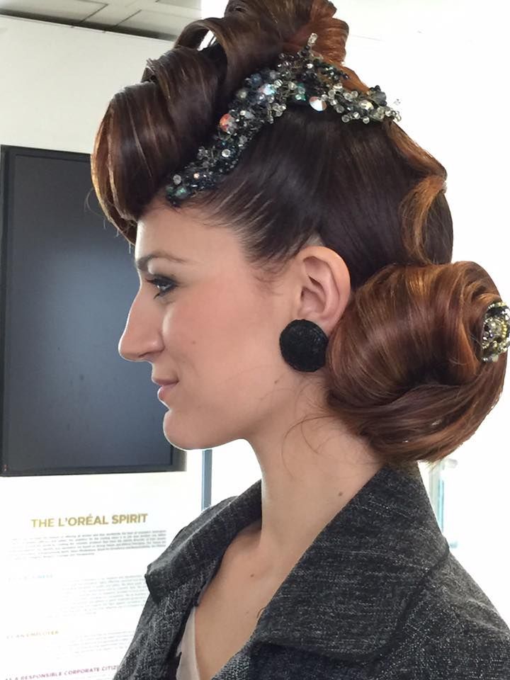 Vue de profil d'une femme arborant une coiffure sophistiquée ornée de bijoux et des boucles d'oreilles foncées, dans un salon de coiffure.