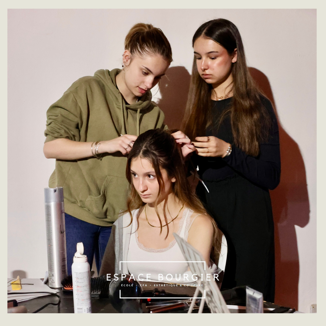 Deux coiffeurs ajustent la coiffure d'un mannequin assis dans un salon, avec des outils de coiffure posés sur la table.