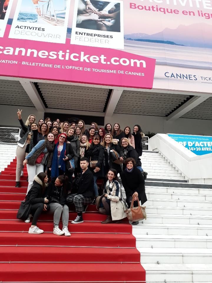 Groupe posant sur des marches recouvertes de tapis rouge sous les panneaux d'affichage des billets pour Cannes à l'entrée d'un immeuble