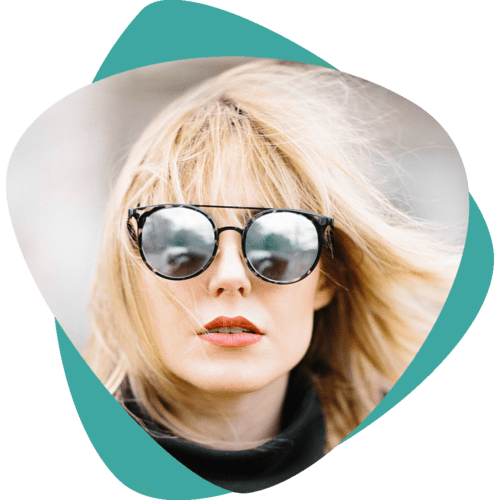 Personne blonde portant des lunettes de soleil rondes et un chapeau blanc sur fond turquoise