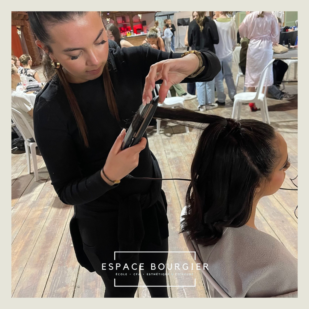 Une coiffeuse lisse les cheveux d'une cliente dans un salon de coiffure avec un fer à lisser.