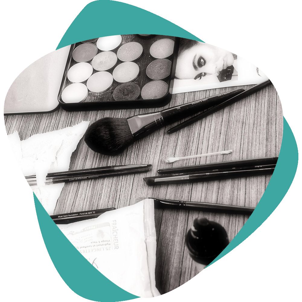Outils et palettes de maquillage en noir et blanc disposés sur une surface en bois avec un motif géométrique turquoise.
