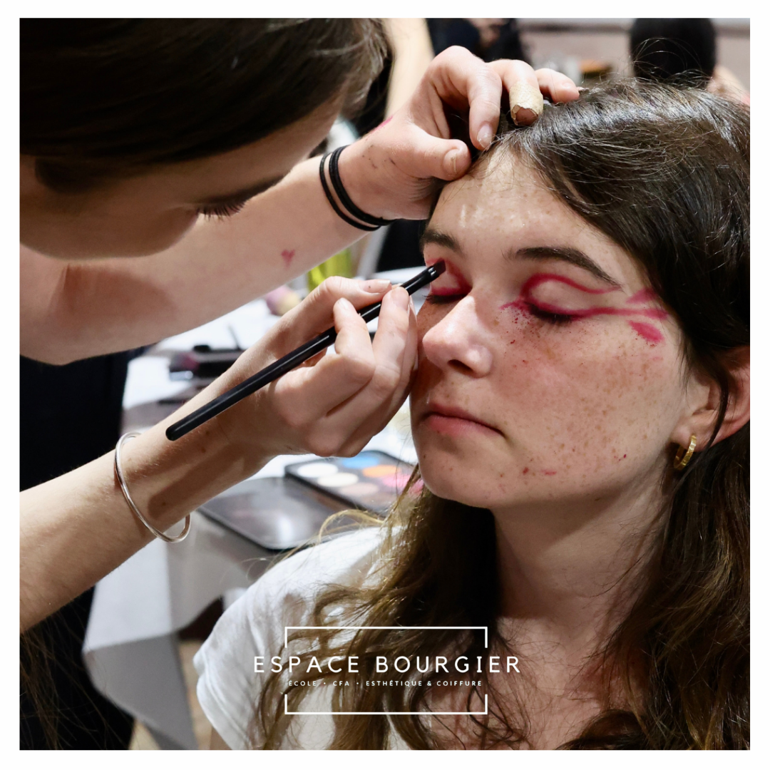 Une maquilleuse applique du maquillage aux yeux d'une femme assise, avec un fard à paupières rose.