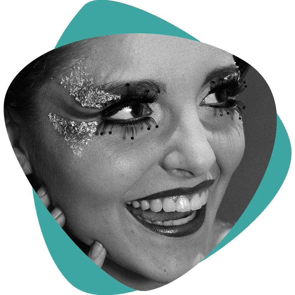 Gros plan en noir et blanc d'un visage souriant avec un maquillage des yeux pailleté sur un fond abstrait turquoise