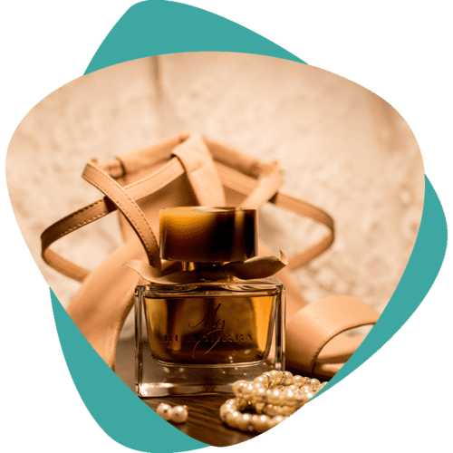 Flacon de parfum ambré orné d'un ruban et de perles sur un fond beige clair, encadré par un cœur turquoise.