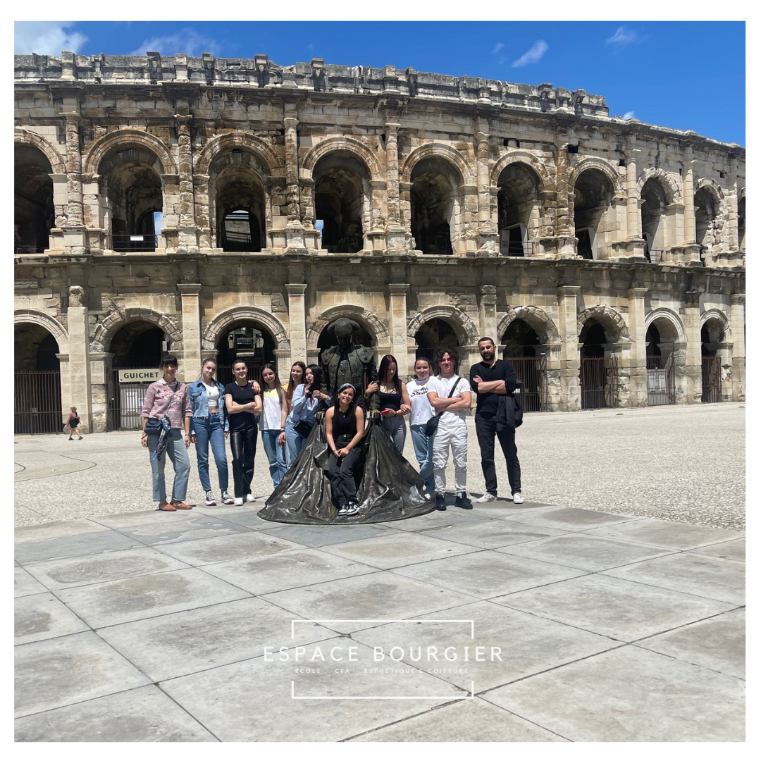 Un groupe de personnes pose devant l'amphithéâtre romain sous un ciel d'un bleu éclatant.