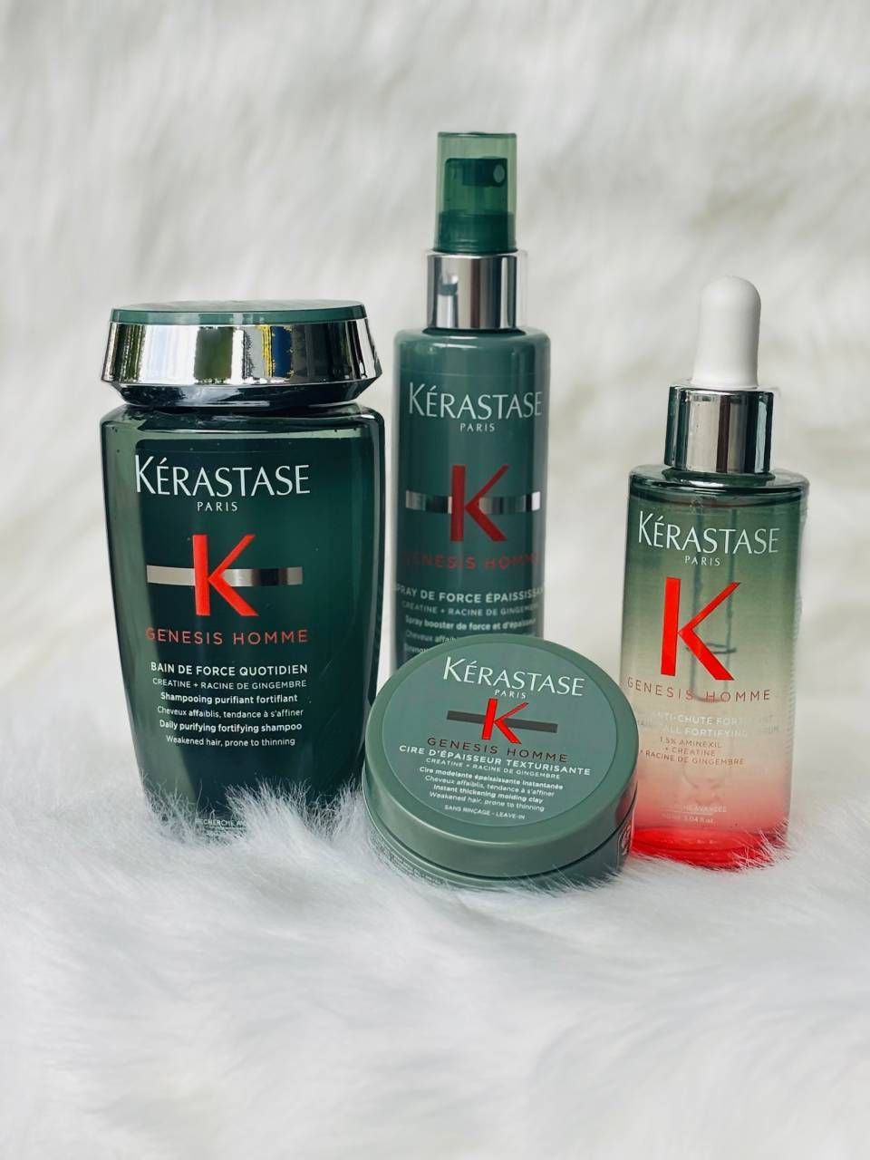 Die Haarpflegeprodukte von Kerastase befinden sich in grünen und silbernen Flaschen auf einer weißen, flauschigen Oberfläche.