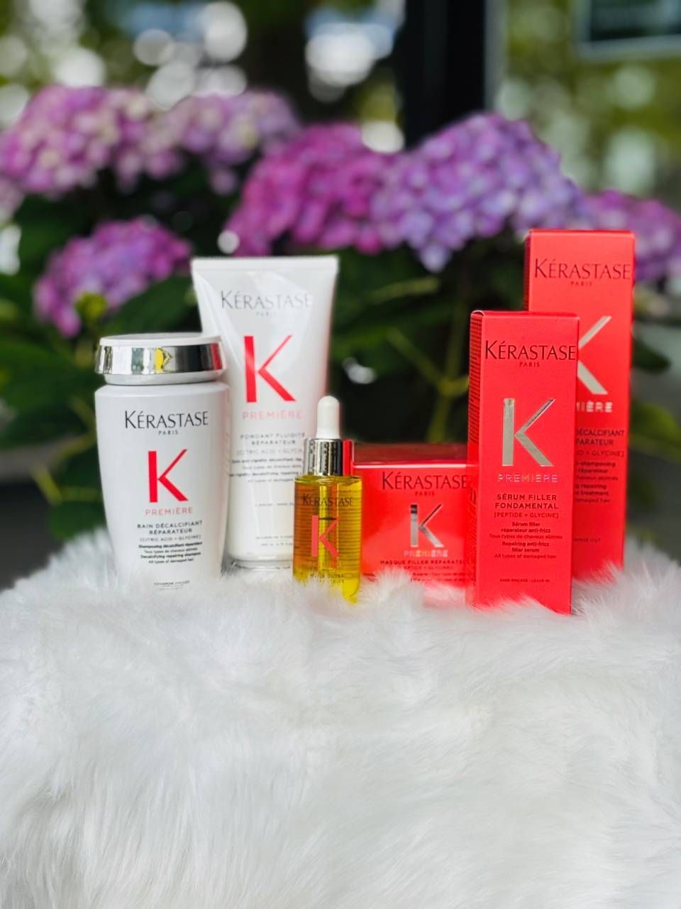 Haarpflegeprodukte in weiß-roter Verpackung auf weißem Untergrund mit verschwommenem floralem Hintergrund.