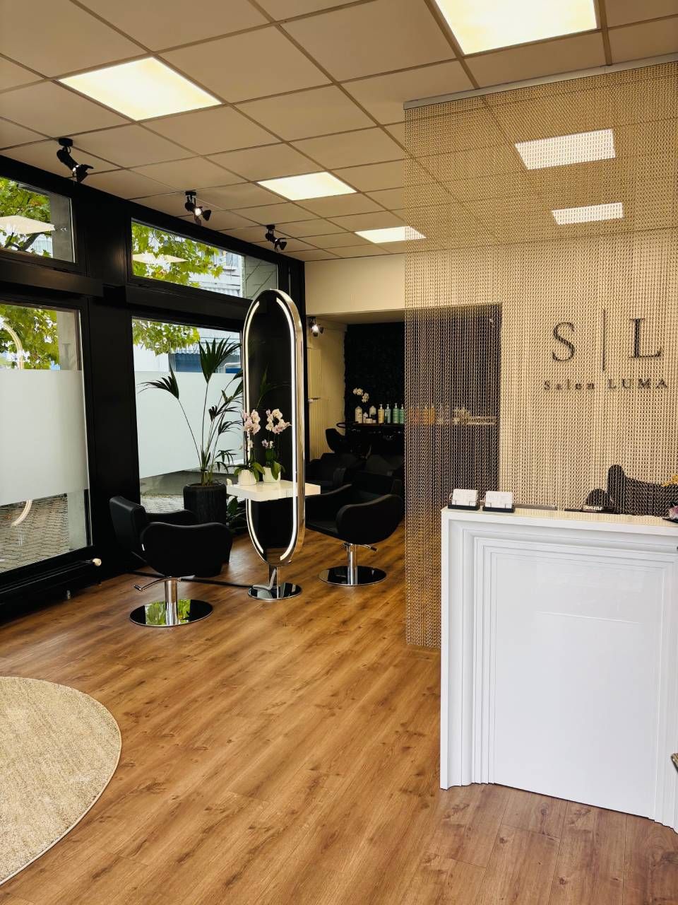 Interieur eines Friseursalons mit Holzböden, schwarzen Stühlen, großen Spiegeln und weißem Empfangstresen.