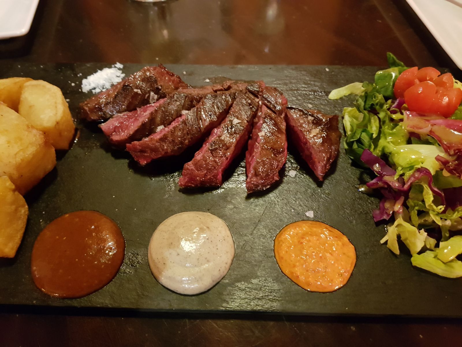 Un plato de comida con carne, verduras y salsas en una mesa.