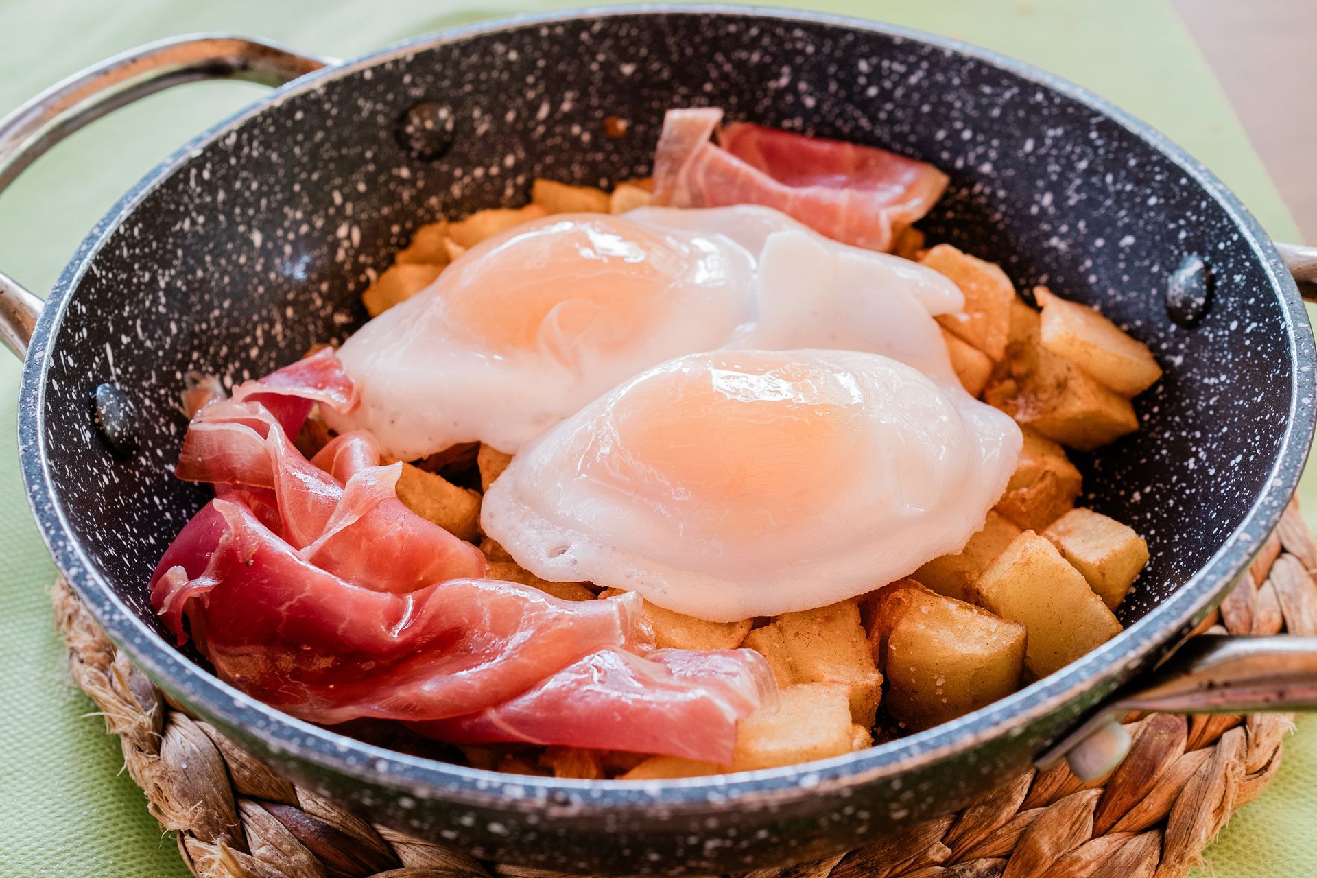 Una sartén llena de huevos, patatas y jamón sobre una mesa.