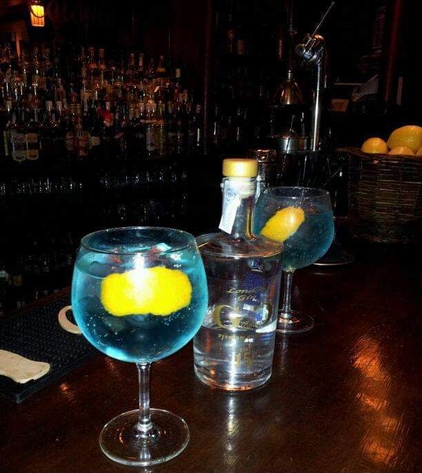 Dos vasos de líquido azul con rodajas de limón en una barra.