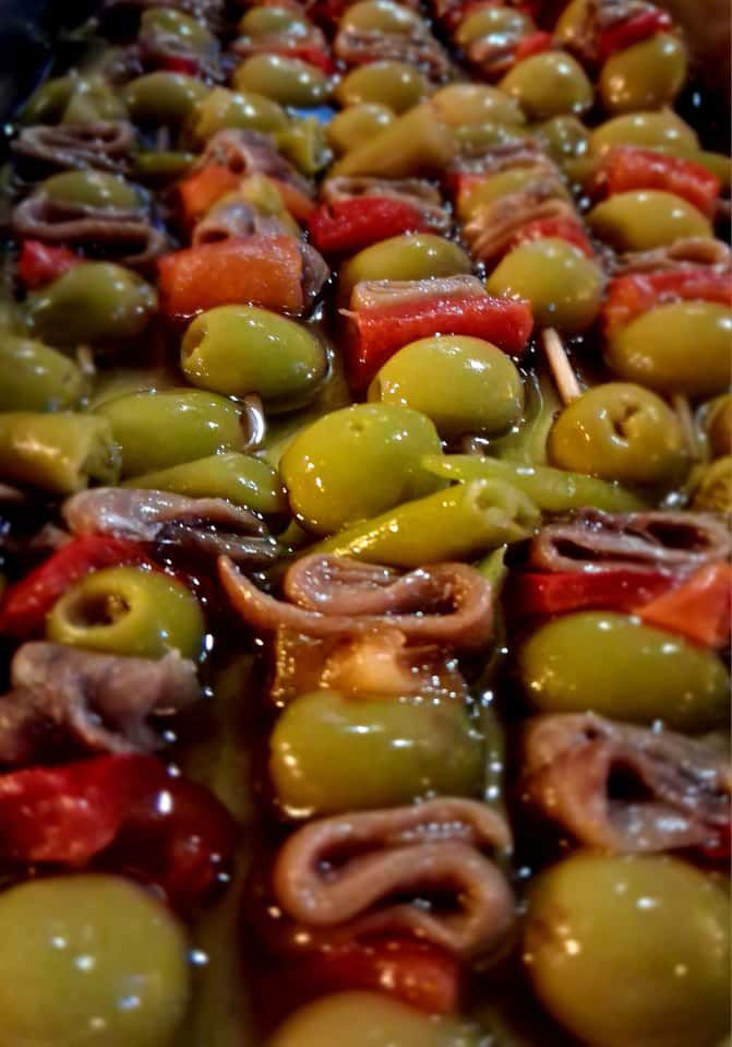Aceitunas variadas en una marinada brillante, primer plano con aceitunas verdes, rojas y negras en un tazón.