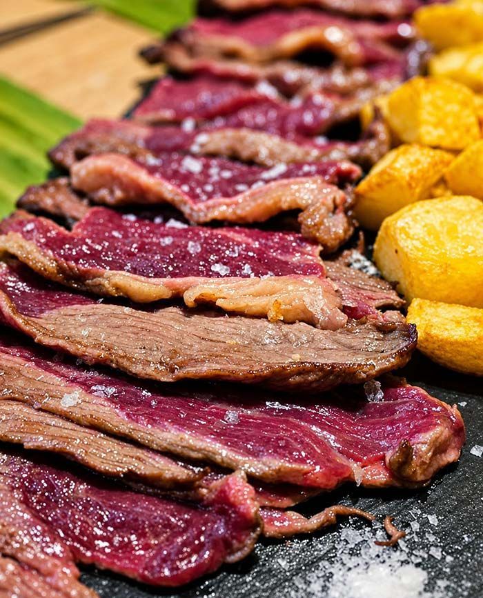 Lonchas de filete sellado sobre una tabla con patatas asadas doradas y verduras.