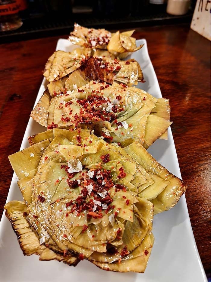 Pasta servida en un plato rectangular blanco, cubierta con queso rallado, hojuelas de pimiento rojo y hierbas.
