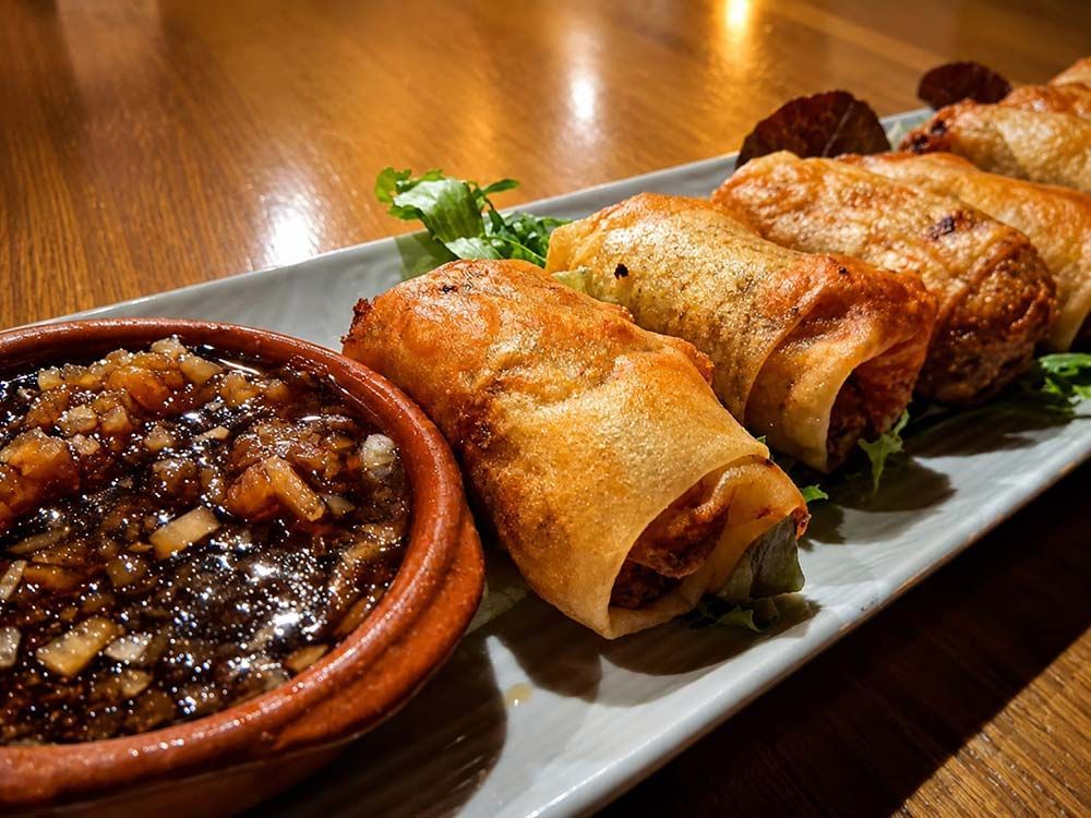 Tres rollitos de primavera fritos y crujientes en un plato con salsa para mojar sobre una mesa de madera.